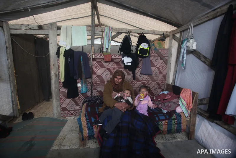 A Palestinian woman sits with her sons, whose house was destroyed in the most recent Israeli offensive on Gaza Strip, during a heavy winter storm, at her a tent in Beit Hanoun in the northern Gaza Strip on January 8, 201...