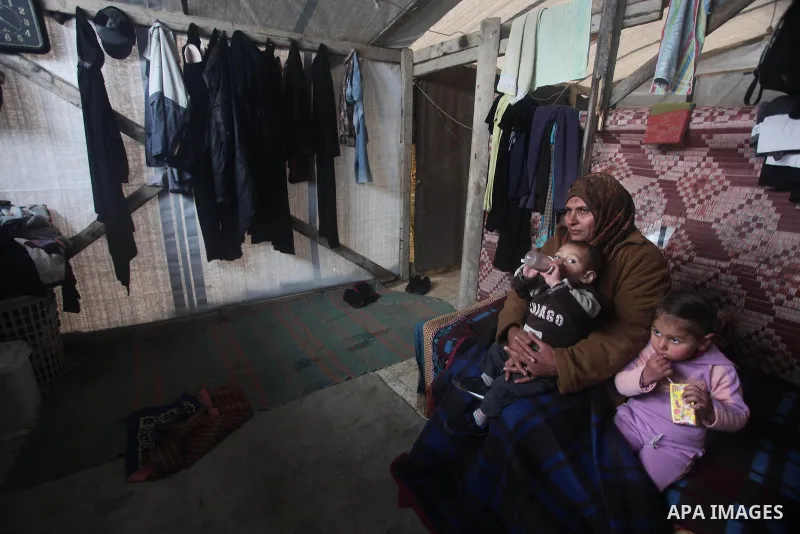 A Palestinian woman sits with her sons, whose house was destroyed in the most recent Israeli offensive on Gaza Strip, during a heavy winter storm, at her a tent in Beit Hanoun in the northern Gaza Strip on January 8, 201...