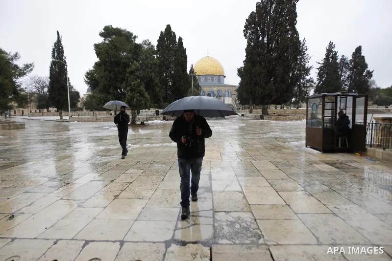 A man holds an umbrella as he walks in front of the Dome of the Rock on the compound known to Muslims as Noble Sanctuary in Jerusalem's Old City after snowfall January 8, 2015. A storm buffeted the Middle East with blizz...
