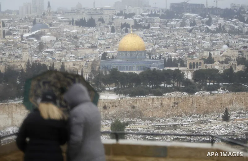 The Dome of the Rock is seen in the background as a tourist holds her umbrella during a gust of wind outside Jerusalem's Old City January 8, 2015. A storm buffeted the Middle East with blizzards, rain and strong winds on...
