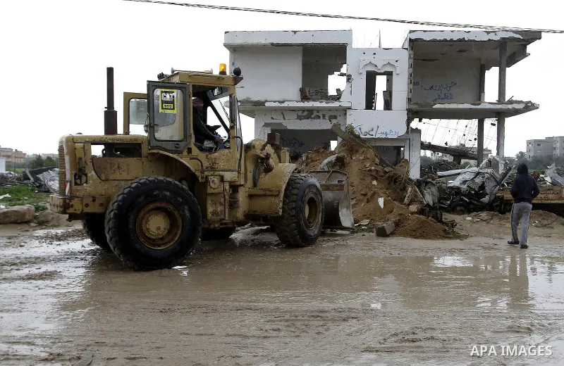 Palestinians, whose houses were destroyed by what they said was Israeli shelling during a 50- day-war last summer, use a bulldozer to remove rubbles on a stormy day in the east of Khan Younis in the southern Gaza Strip J...