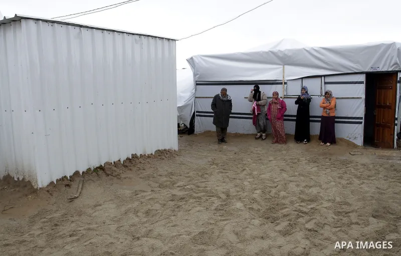 Palestinians, whose houses were destroyed by what they said was Israeli shelling during a 50- day-war last summer, stand outside containers used as temporary replacement for their damaged homes, on a stormy day in the ea...