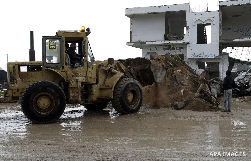 Palestinians, whose houses were destroyed by what they said was Israeli shelling during a 50- day-war last summer, use a bulldozer to remove rubbles on a stormy day in the east of Khan Younis in the southern Gaza Strip J...
