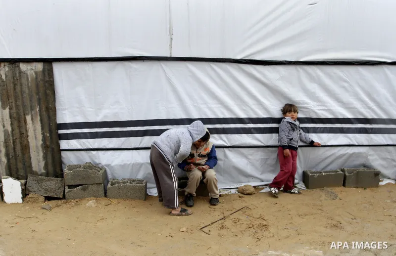 Palestinian children, whose houses were destroyed by what they said was Israeli shelling during a 50- day-war last summer, play outside a container used as temporary replacement for their damaged homes, on a stormy day i...