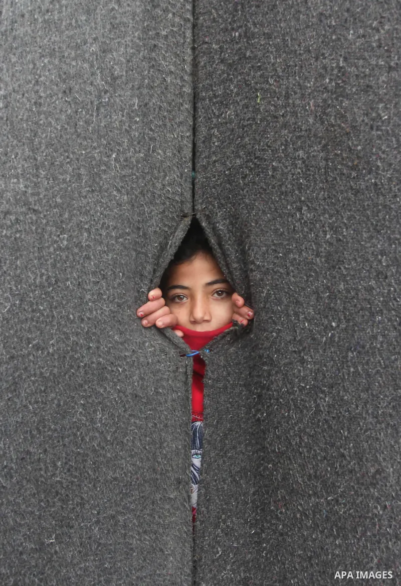 A Palestinian girl looks on behind a curtain at a United Nations (UN) run school sheltering Palestinians, whose houses were destroyed in the 50- day-war Israeli last summer, during a winter storm in Beit Hanoun in the no...