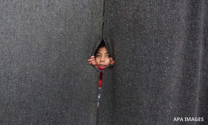 A Palestinian girl looks on behind a curtain at a United Nations (UN) run school sheltering Palestinians, whose houses were destroyed in the 50- day-war Israeli last summer, during a winter storm in Beit Hanoun in the no...