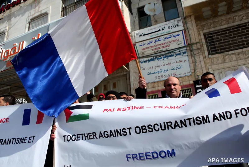 Palestinians and French protestors wave their national flags during a gathering in front of the Hebron-France Association for Cultural Exchange in the West Bank town of Hebron on January 10, 2015 as they demonstrate agai...