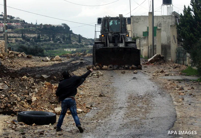 A Palestinian protester throws stones towards Israeli bulldozer during clashes following a protest against the expropriation of Palestinian land by Israel, in the village of Kafr Qaddum, near the West Bank city of Nablus...