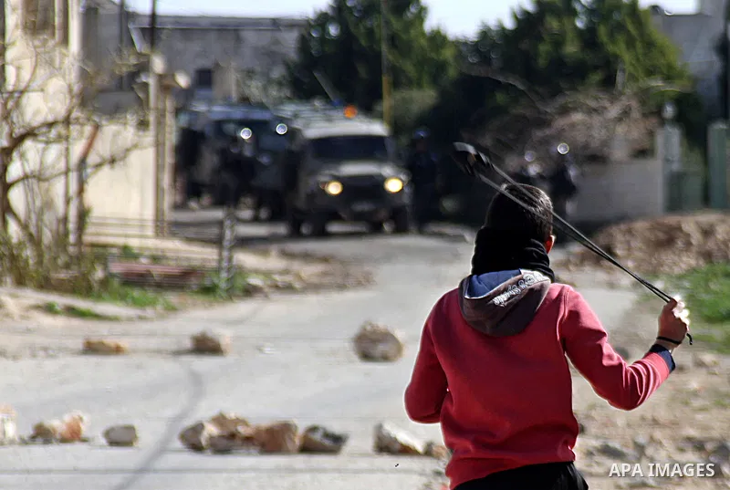 A Palestinian protester uses a slingshot to throw a stone towards Israeli security forces during clashes following a demonstration against the expropriation of Palestinian land by Israel in the village of Kfar Qaddum, ne...