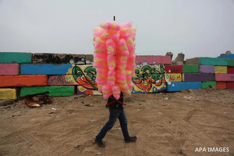 A Palestinian man sells a sweets past a big stone wall on January 25, 2015 that was painted by local artists at the sea port in Gaza City in an attempt to bring more vibrant colours to the city. Photo by Ashraf Amra