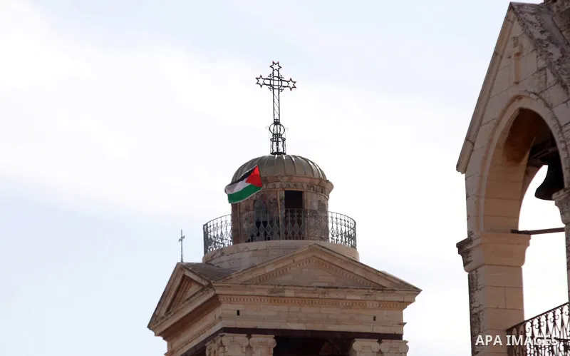 A Palestinian Christian man waves Palestinian flag on the Church of the Nativity, in protest against Patriarch Theophilos III of Jerusalem, in the West Bank city of Bethlehem on January 25, 2015. Palestinians hold a camp...