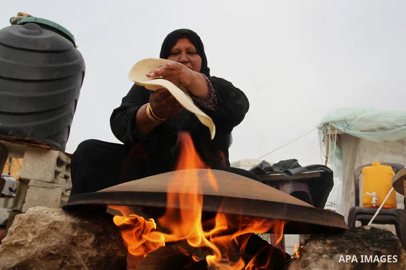 A Palestinian woman bakes bread on firewood outside a tent near the ruins of her house which witnesses said were destroyed by Israel shelling during a 50-day conflict last summer, east of Khan Younis in the southern Gaza...