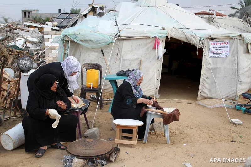 Palestinian women bake bread on firewood outside a tent near the ruins of their houses which witnesses said were destroyed by Israel shelling during a 50-day conflict last summer, east of Khan Younis in the southern Gaza...