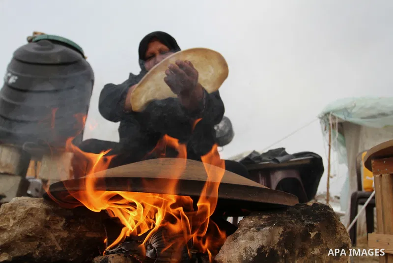 A Palestinian woman bakes bread on firewood outside a tent near the ruins of her house which witnesses said were destroyed by Israel shelling during a 50-day conflict last summer, east of Khan Younis in the southern Gaza...