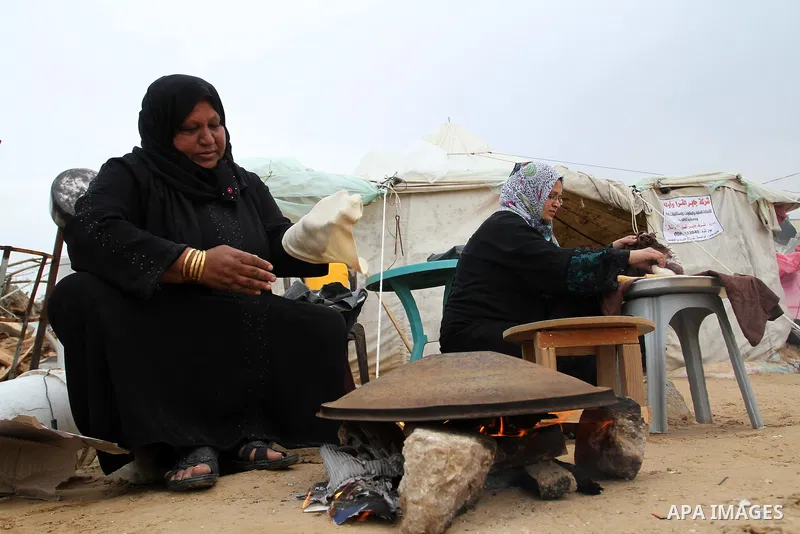 Palestinian women bake bread on firewood outside a tent near the ruins of their houses which witnesses said were destroyed by Israel shelling during a 50-day conflict last summer, east of Khan Younis in the southern Gaza...