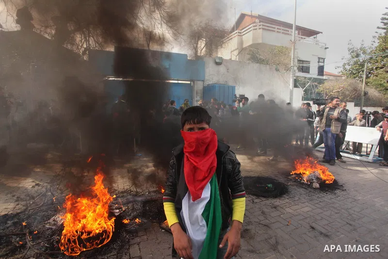 A Palestinian boy stands near burning tyres during a protest against the decision by the main U.N. aid agency to suspend payments to tens of thousands of Palestinians for repairs to their homes damaged in last summer's w...