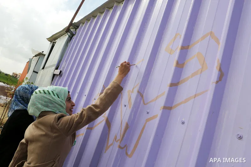 Palestinian girls paint a container of a family, which their house was destroyed by Israeli shelling during a 50-day conflict last summer, east if Khan Younis in the southern Gaza Strip, January 28, 2015. Dozens of prote...