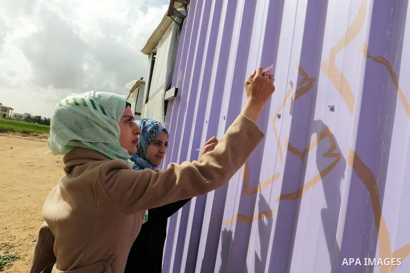 Palestinian girls paint a container of a family, which their house was destroyed by Israeli shelling during a 50-day conflict last summer, east if Khan Younis in the southern Gaza Strip, January 28, 2015. Dozens of prote...