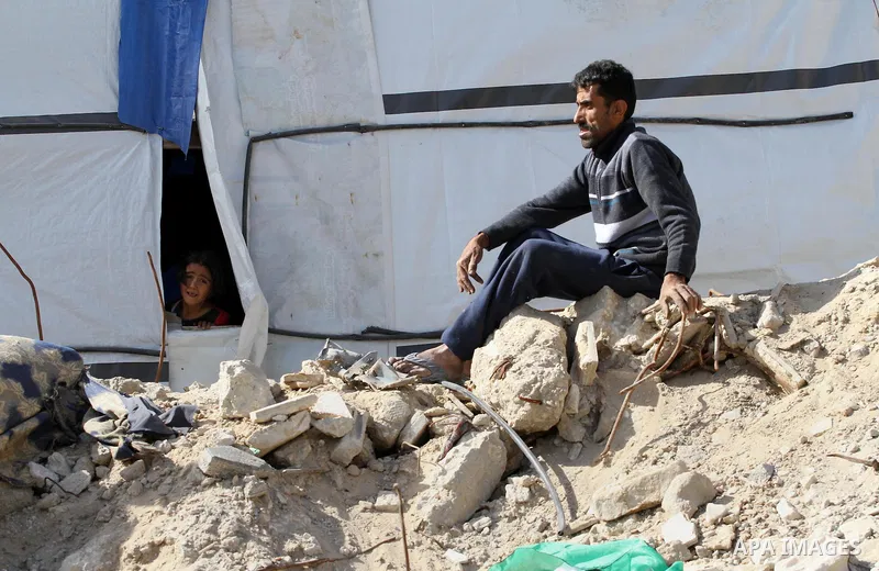 A Palestinian man sits on the rubbles of his destroyed house as his daughter looks on from a tent during a protest against the United Nations decision to suspend payments for Palestinians, whose houses were damaged durin...
