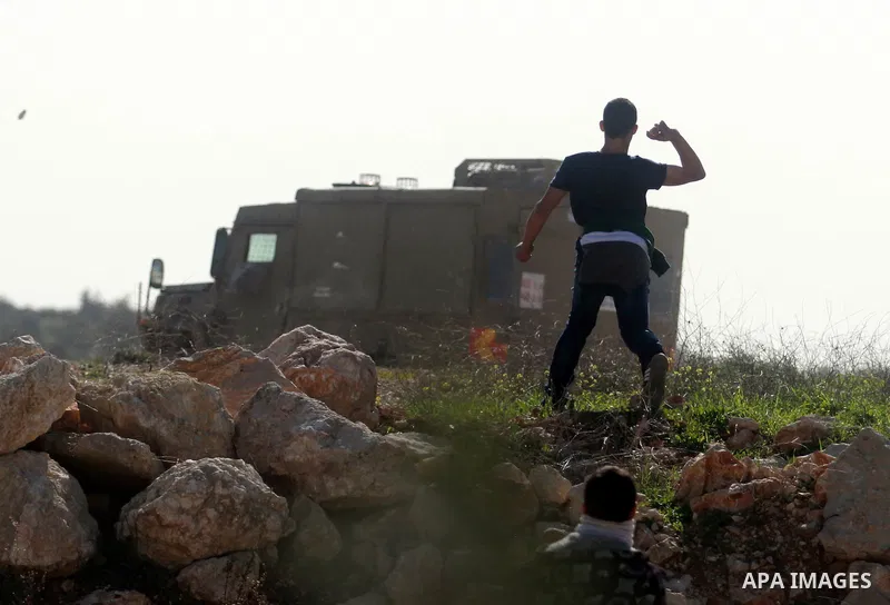A Palestinian protester throws stones towards Israeli security forces during clashes following a protest against the arrest of 14-year-old girl Malak al-Khatib, in the West Bank village of Bilin west of Ramallah, on Janu...
