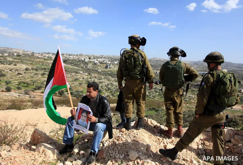 A Palestinian protester holds a portrait of Malak al-Khatib, 14, who was arrested for throwing stones, in front of Israeli security forces during a protest against her detention by Israel, in the West Bank village of Bil...