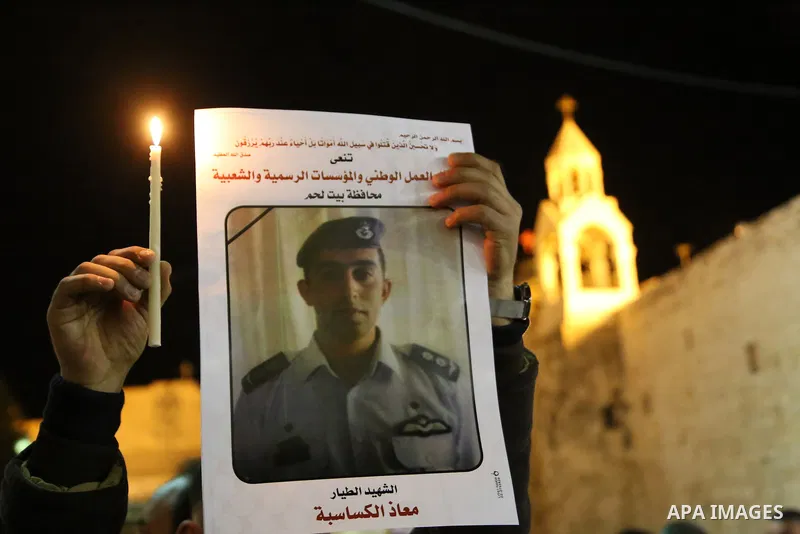 A Palestinian man holds a candle and portrait of slain Jordanian pilot, Lt. Muath al-Kasasbeh, killed by the Islamic State group, during a candle light vigil outside the Nativity Church in the West Bank city of Bethlehem...