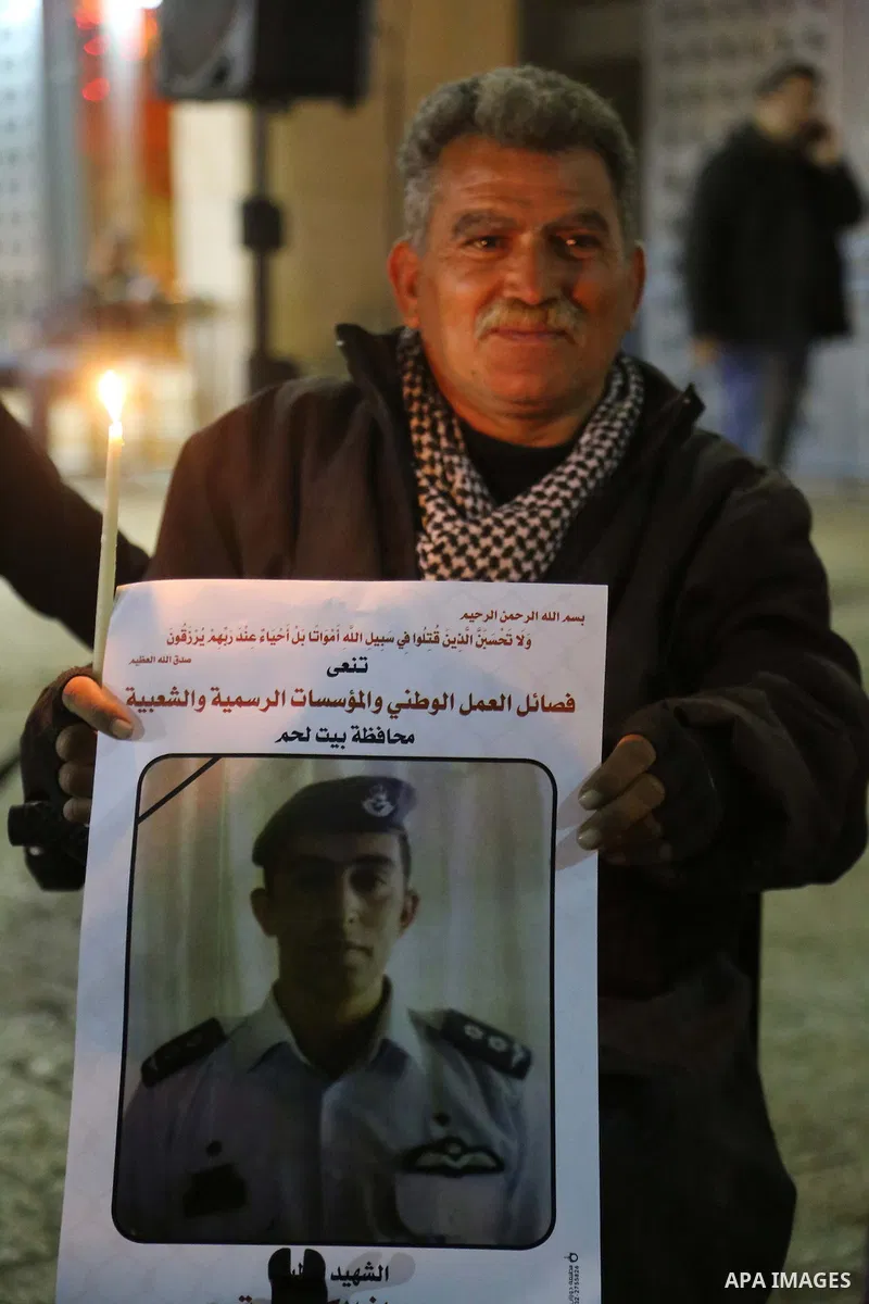 A Palestinian man holds a candle and portrait of slain Jordanian pilot, Lt. Muath al-Kasasbeh, killed by the Islamic State group, during a candle light vigil outside the Nativity Church in the West Bank city of Bethlehem...