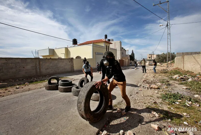 A masked Palestinian protester pushes a tire during clashes with Israeli security forces following a demonstration against the expropriation of Palestinian land by Israel in the village of Kfar Qaddum, near Nablus in the...