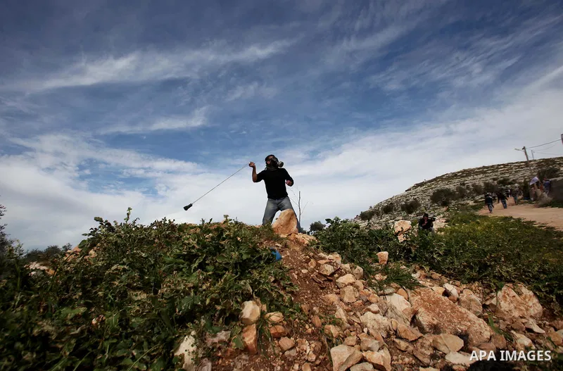 A Palestinian youth uses a sling shot to hurl a stone at Israeli security forces during clashes following a demonstration against the expropriation of Palestinian land by Israel in the village of Kfar Qaddum, near Nablus...