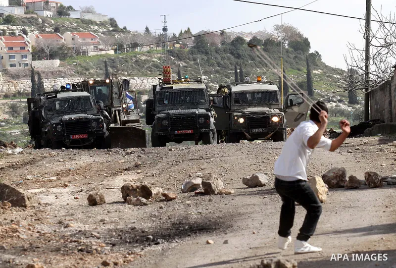 A Palestinian youth uses a sling shot to hurl a stone at Israeli security forces during clashes following a demonstration against the expropriation of Palestinian land by Israel in the village of Kfar Qaddum, near Nablus...