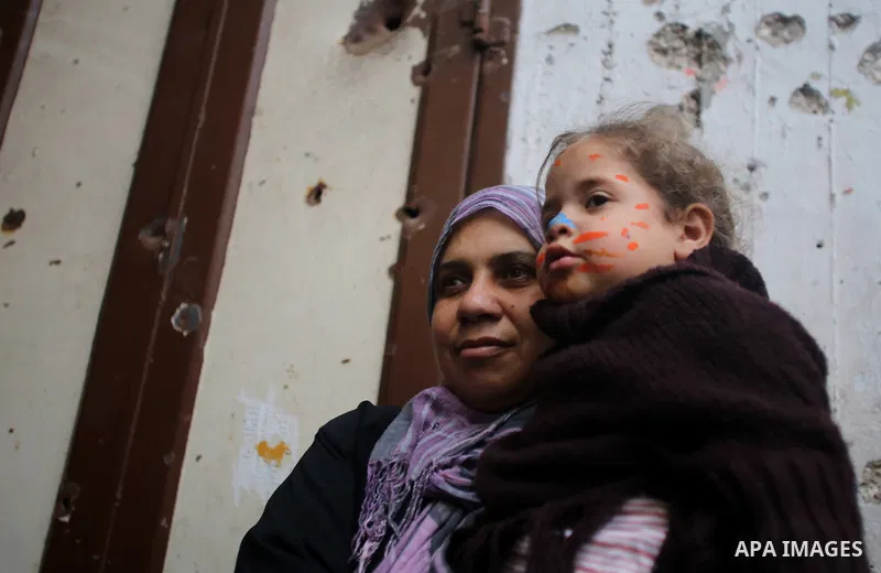 A Palestinian woman carries her daughter during a street game organised by volunteers of the Friday of Joy Initiative, in al-Shati refugee camp, in Gaza city, February 6, 2015. Ten Palestinian volunteers organise street...