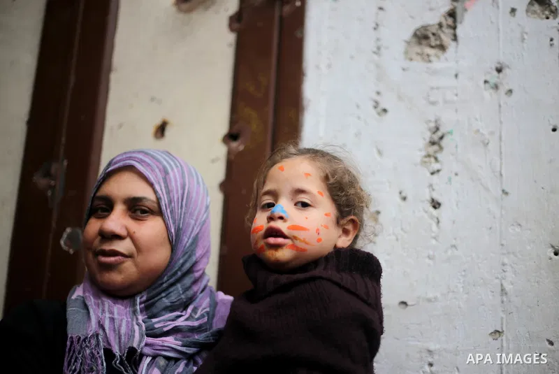A Palestinian woman carries her daughter during a street game organised by volunteers of the Friday of Joy Initiative, in al-Shati refugee camp, in Gaza city, February 6, 2015. Ten Palestinian volunteers organise street...