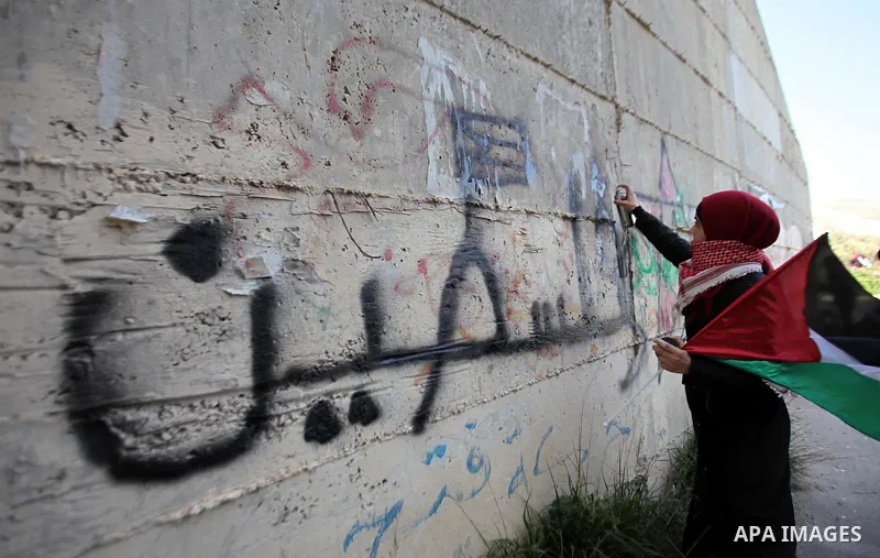 A Palestinian woman writes slogans on the wall during a protest at the scene where Ahmed al-Najjar by Israeli soldiers on January 30, 2015, in the West Bank village of Burin, near Nablus on February 7, 2015. Local source...
