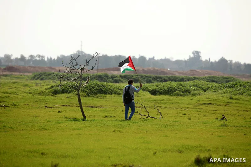 A Palestinian protestor waves his national flags during a protest against the Israeli siege on Gaza strip near the Nahal Oz crossing east of Gaza City on February 09, 2015. Photo by Ashraf Amra