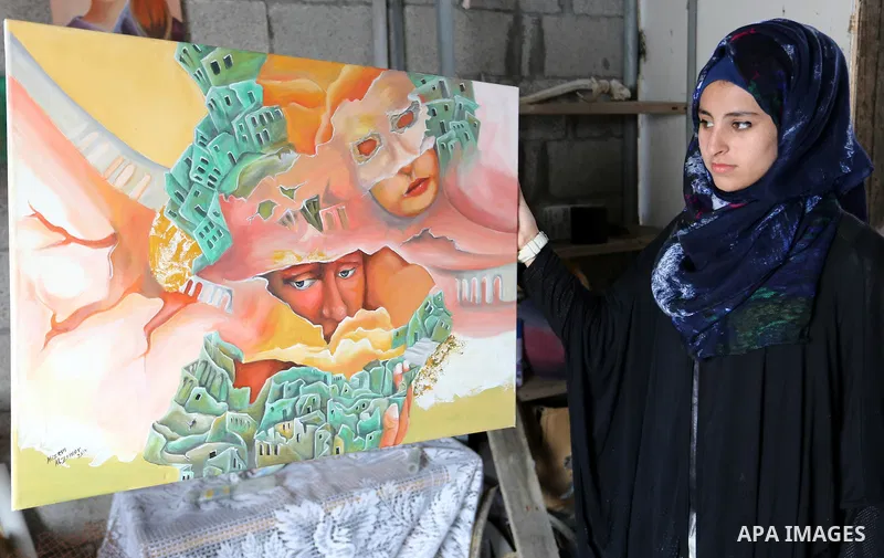 A Palestinian girl displays a painting at an atelier in Rafah in the southern Gaza Strip, February 9, 2015. Three Palestinian artists use the remains of houses which were destroyed during the 51 day Israeli recent war on...