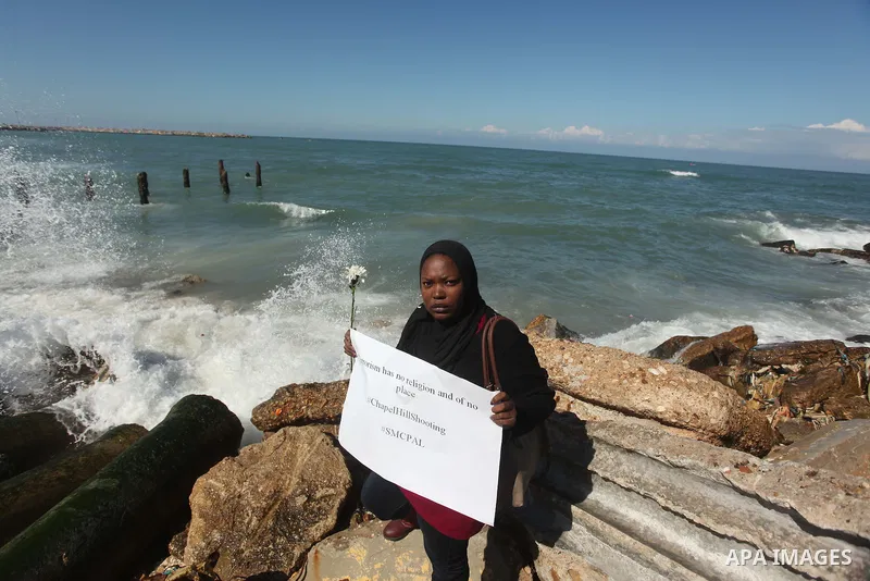A Palestinian woman carries flowers gathers at the sea of Gaza City, on February 14, 2015. Three young Muslims were gunned down in Chapel Hill, North Carolina, this week. Newlywed Deah Shaddy Barakat, 23, a University of...