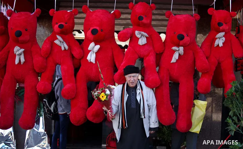 A Palestinian man holds flowers in front of a shop displaying red teddy bears on Valentine's day in Gaza on February 14, 2015. Valentine's Day is increasingly popular in the region as people have taken up the custom of g...