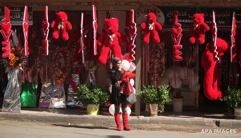 A Palestinian girl holds flowers in front of a shop displaying red teddy bears on Valentine's day in Gaza on February 14, 2015. Valentine's Day is increasingly popular in the region as people have taken up the custom of...