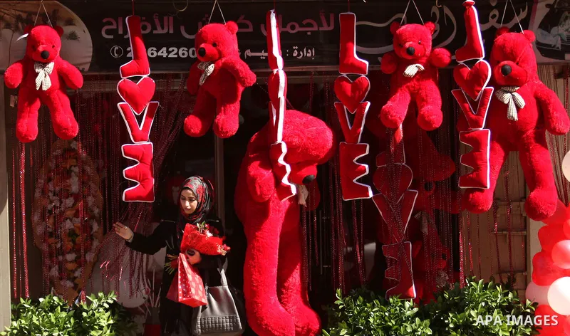 A Palestinian girl holds flowers in front of a shop displaying red teddy bears on Valentine's day in Gaza on February 14, 2015. Valentine's Day is increasingly popular in the region as people have taken up the custom of...