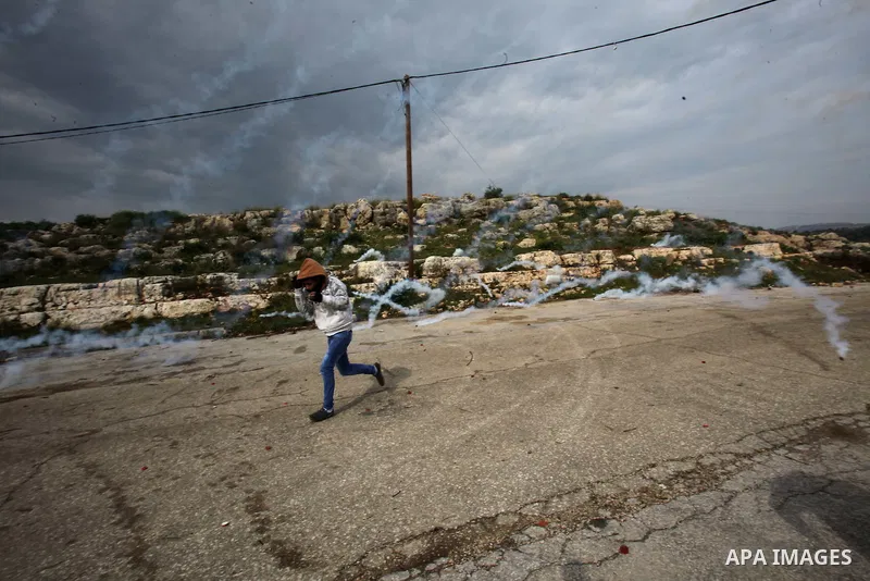 A Palestinian Protester runs away from tear gas fired by Israeli border policemen during clashes following a protest against closure of the village road, in the West Bank village of Azzun near Qalqilya February 14, 2015....