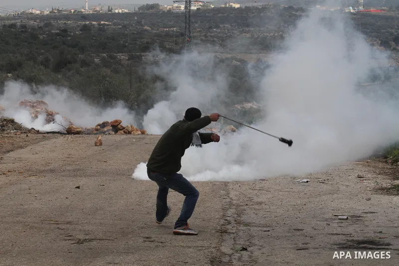 A Palestinian protester throws back a tear gas canister fired by Israeli border policemen during clashes following a protest against closure of the village road, in the West Bank village of Azzun near Qalqilya February 1...