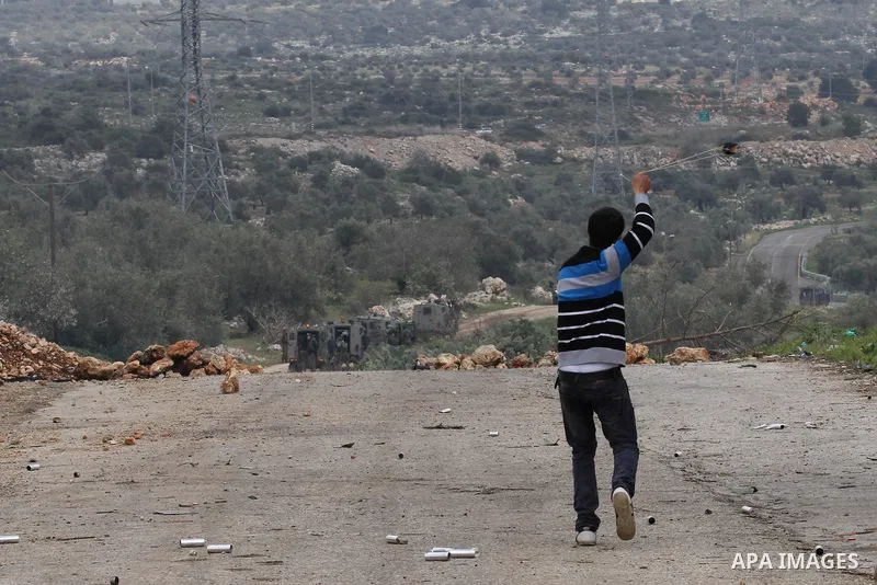 A Palestinian protester uses a sling shot to throw stones towards Israeli border policemen during clashes following a protest against closure of the village road, in the West Bank village of Azzun near Qalqilya February...