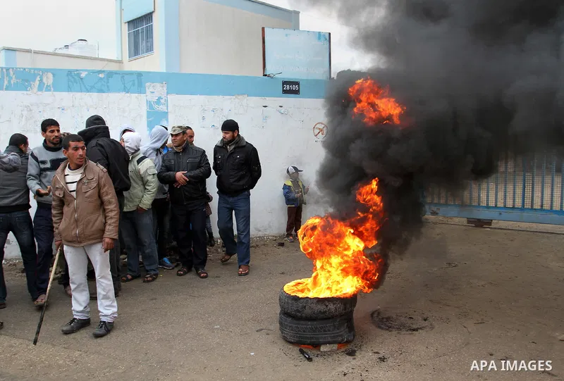 Smoke rises from burning tyres as Palestinians shout during a protest calling for reconstruction of their houses that witnesses said were destroyed by Israeli shelling during a 50-day war last summer, outside a United Na...