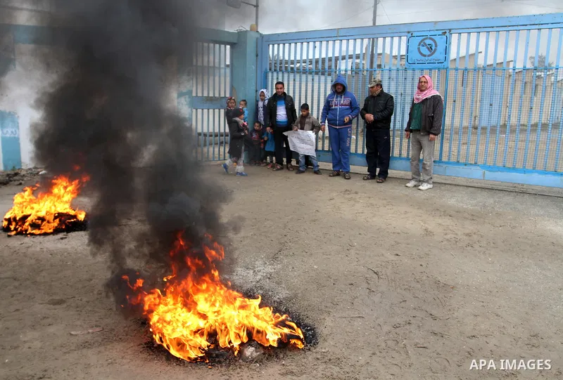 Smoke rises from burning tyres as Palestinians shout during a protest calling for reconstruction of their houses that witnesses said were destroyed by Israeli shelling during a 50-day war last summer, outside a United Na...