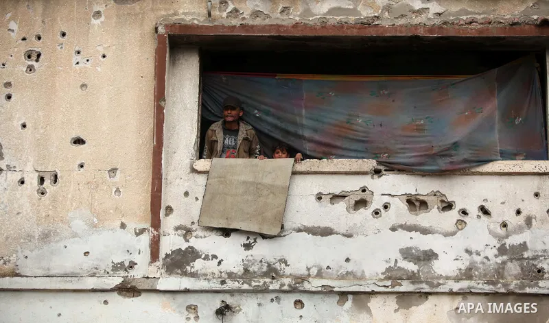 A Palestinian man with his child look on from his house, which was damaged during the recent Israeli war, in Shejaiya neighborhood in Gaza city, February 18, 2015. At least 100,000 Palestinians are still living without a...