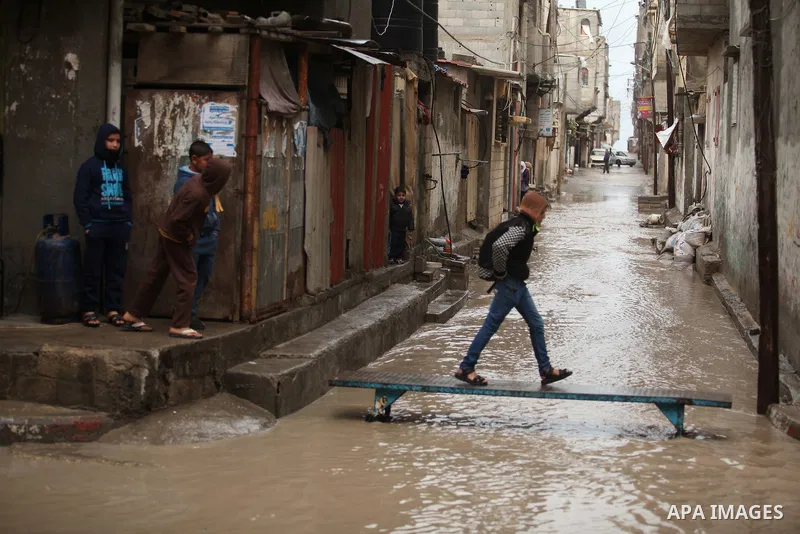 Palestinian students walk in a flooded street during a rainy day at Shati refugee camp in Gaza City, Feb. 19, 2015. Photo by Ashraf Amra