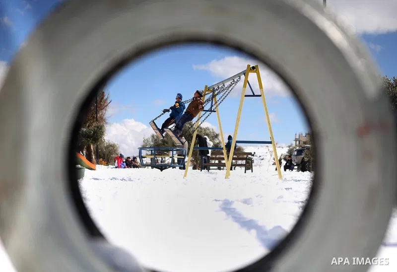 Palestinian children play at a parl as smpw falls in the West Bank city of Ramallah February 20, 2015. A heavy winter storm hit parts of the Middle East on Friday, shutting down roads leading in and out of Jerusalem and...