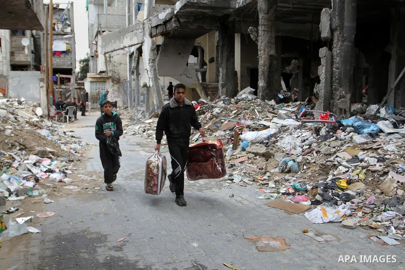A Palestinian boy carries belongings as he walks past the rubbles of houses, which was damaged during the recent Israeli war, in Rafah in the southern Gaza strip, February 22, 2015. At least 100,000 Palestinians are stil...