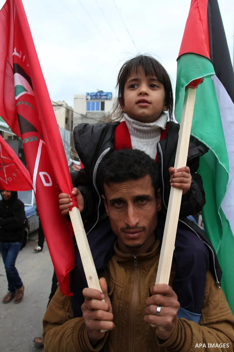 A Palestinian man carries his son during a rally marking the 46th anniversary of the founding of the Democratic Front for the Liberation of Palestine (DFLP), in Rafah in the southern Gaza Strip February 23, 2015. Photo b...