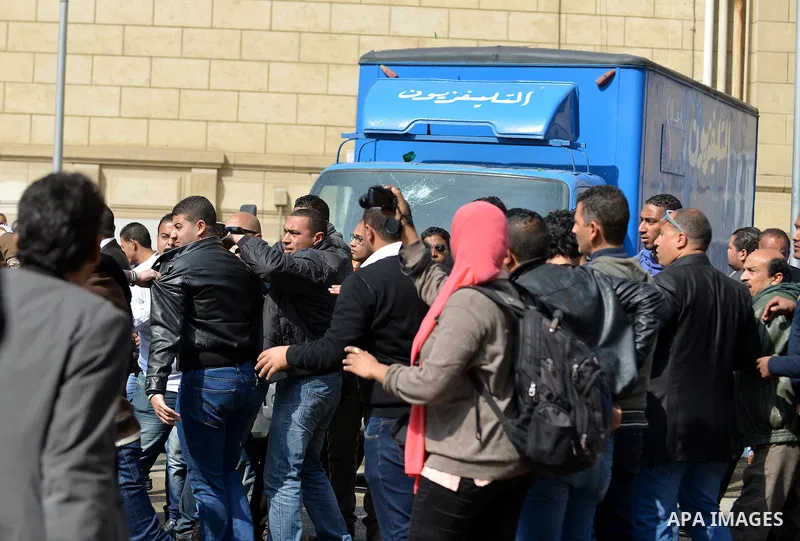 Egyptians gather arround a car belong to the Egyptian television after it was broken by students who are support ousted President Mohamed Morsi and the Muslim Brotherhood during protest against the military rule, in Cair...
